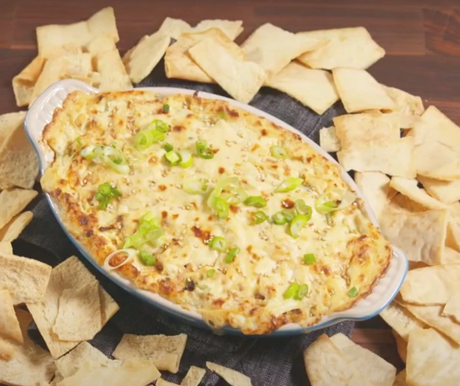 reamy Crab Rangoon Dip served in a white baking dish with golden melted cheese topping, garnished with green onions, and surrounded by crispy wonton chips.