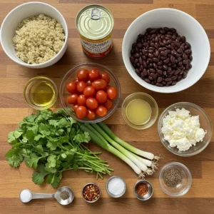 Fresh ingredients for a quinoa salad bowl, including quinoa, cherry tomatoes, black beans, cilantro, and lime, neatly arranged on a wooden surface.