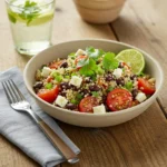 A beautifully plated quinoa salad bowl, garnished with fresh herbs and served with a side of lemon wedges.