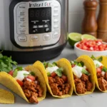 Instant Pot open on a kitchen counter, filled with fresh tacos topped with cilantro and tomatoes.