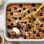 Blueberry-Coconut-Walnut Baked Oatmeal in a white dish topped with fresh blueberries, coconut flakes, and walnuts.